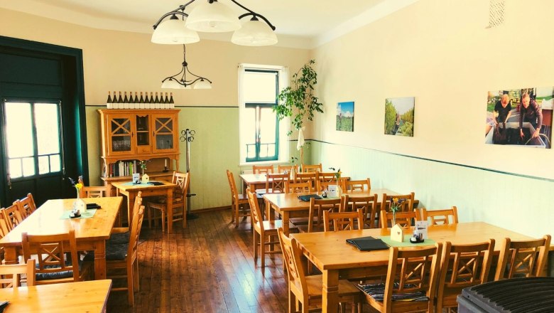 Gastzimmer, © Weingut Hess Ein gemütlicher Gastraum mit Holztischen und -stühlen, dekoriert mit Weinflaschen und Bildern an der Wand.