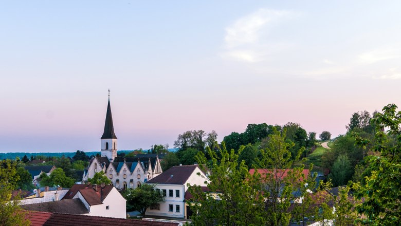 Jedenspeigen, © Gemeinde Jedenspeigen Blick auf die Kirche von Jedenspeigen bei Sonnenuntergang, umgeben von Bäumen und Häusern.