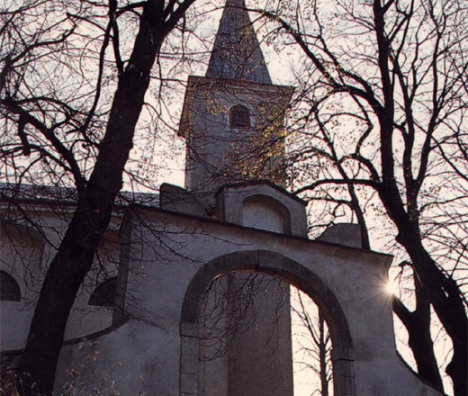 Wallfahrtskirche am Heiligen Berg, © Wallfahrtskirche Kirche mit Turm und Bogen, umgeben von kahlen Bäumen im Gegenlicht.