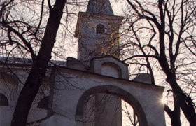 Wallfahrtskirche am Heiligen Berg, © Wallfahrtskirche Kirche mit Turm und Bogen, umgeben von kahlen Bäumen im Gegenlicht.