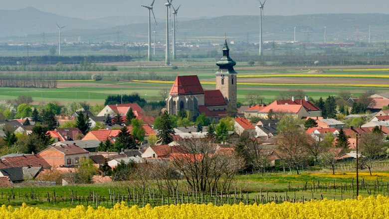 Pillichsdorf, © Thomas Falch Blick auf Pillichsdorf mit Kirche, umgeben von Feldern und Windrädern im Hintergrund.