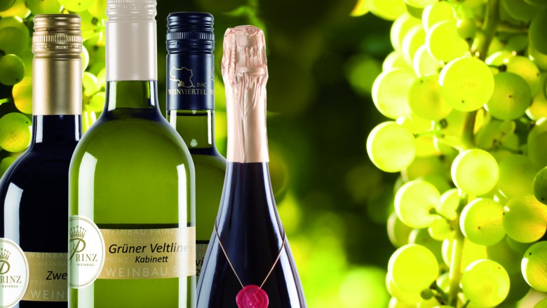 Wein aus dem Weinviertel, © Weinbau Prinz Weinflaschen vor einem Hintergrund aus grünen Weintrauben.