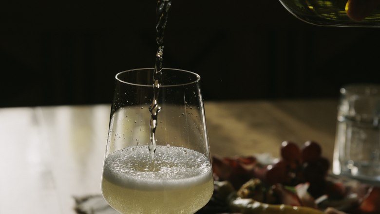 Wein einschenken, © Weinviertel Tourismus / Sophie Menegaldo Ein Glas Weißwein wird auf einem Tisch eingeschenkt, im Hintergrund ein Teller mit Snacks.