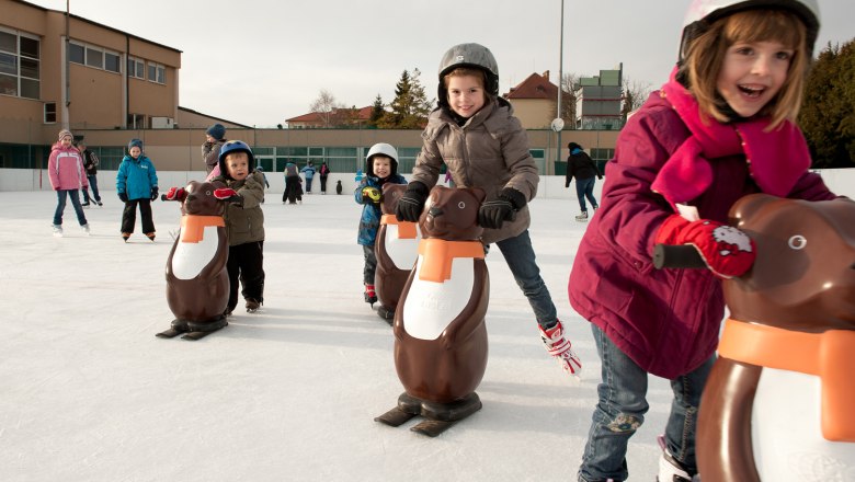 Matzen, © Barbara P. Photography Kinder beim Schlittschuhlaufen mit Pinguin-Hilfen auf einer Eisbahn.