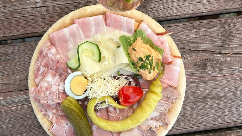 Heurigengenuss, © Weingut Döllinger Ein Teller mit Aufschnitt, Käse, Ei, Gurke, Paprika und Brotaufstrich auf einem Holztisch. Daneben ein Glas Roséwein mit Strohhalm.