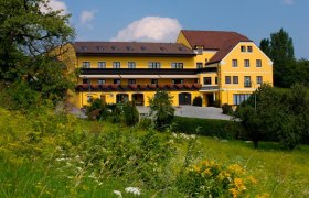 Hotel Stich, © Familie Stich Gelbes Hotelgebäude mit Blumenbalkonen, umgeben von grüner Landschaft.