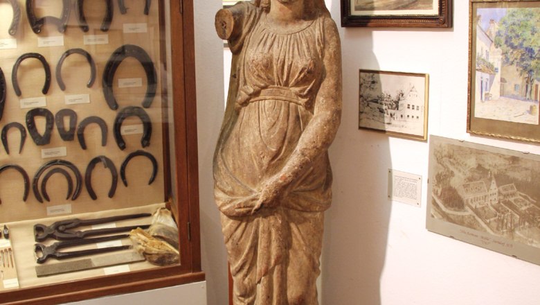 Belvedereschlössl/Bezirksmuseum Stockerau, © Stadtgemeinde Stockerau Innenansicht eines Museums mit antiker Statue, Hufeisen in einer Vitrine und historischen Bildern an der Wand.