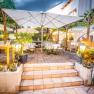 TDR-Gastgarten Hopfeld Dreikönigshof, © flotographix -Kampl Florian Gemütlicher Gastgarten mit Tischen, Stühlen und Sonnenschirmen, umgeben von Pflanzen und Lichtern.