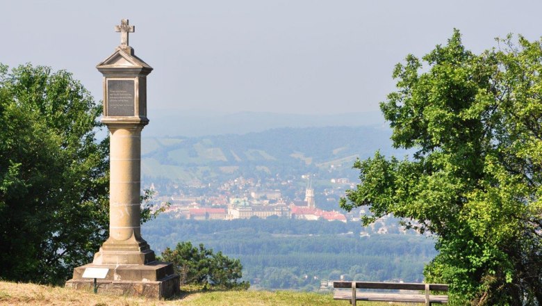 Bisamberg, © Gemeinde Bisamberg Säule mit Kreuz auf einem Hügel, im Hintergrund eine Stadt und Hügel.