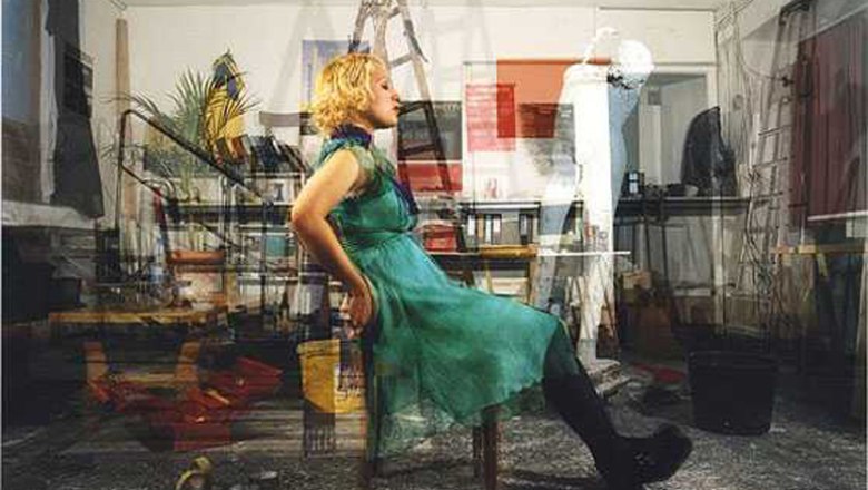 Weinviertler Fotowochen, © FLUSS / John Hilliard Eine Frau in einem grünen Kleid sitzt in einem überfüllten Raum auf einem Stuhl.