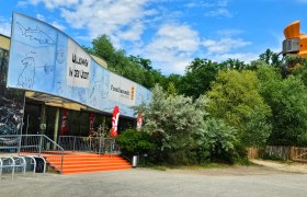 Herzlich Willkommen, © Fossilienwelt Eingang der Fossilienwelt mit einem großen Banner und Bäumen im Hintergrund.