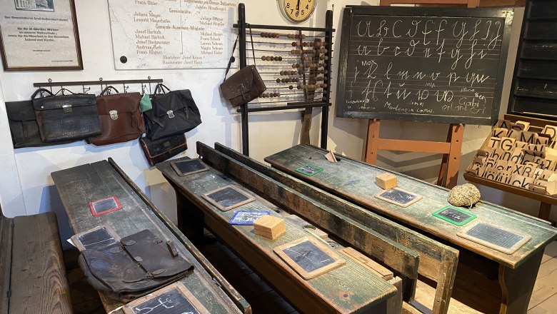 Historisches Klassenzimmer mit alten Holzb&auml;nken, Schiefertafeln und einer Tafel mit Schreib&uuml;bungen.