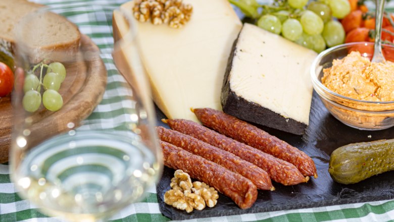 Picknicktisch mit K&auml;se, Wurst, Brot, Weintrauben und einem Glas Wei&szlig;wein.