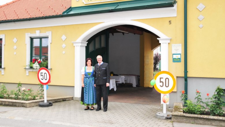 Ein Paar steht vor einem gelben Gebäude mit der Aufschrift 'Weinbau Haller'.