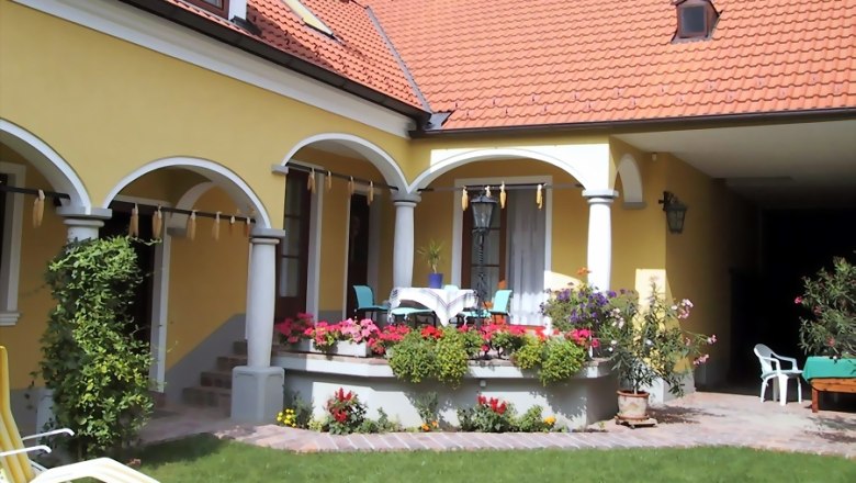 Gelbes Haus mit rotem Dach, Arkaden und Terrasse mit Blumen.
