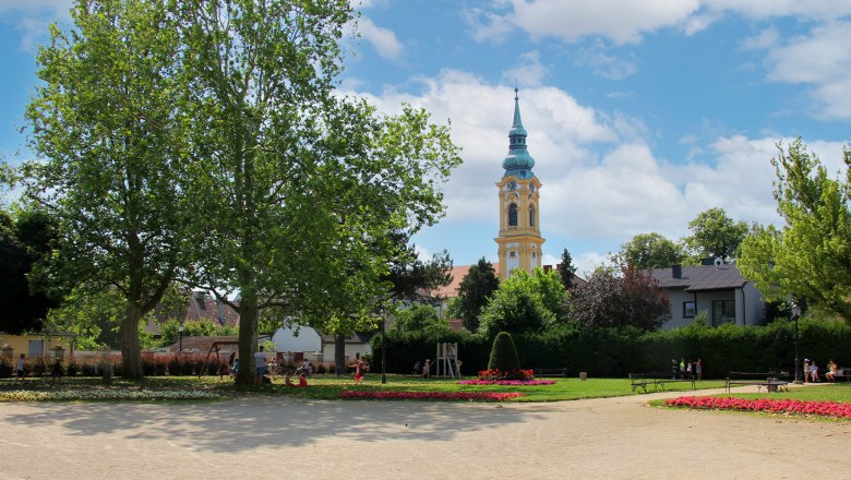 Ein Park mit Blumenbeeten, Bäumen und einem Kirchturm im Hintergrund.
