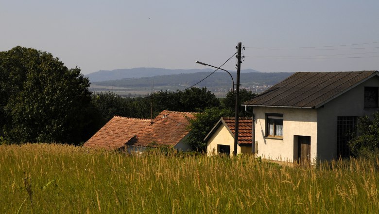 L&auml;ndliche Szene mit H&auml;usern und Wiesen im Vordergrund, H&uuml;gel im Hintergrund.