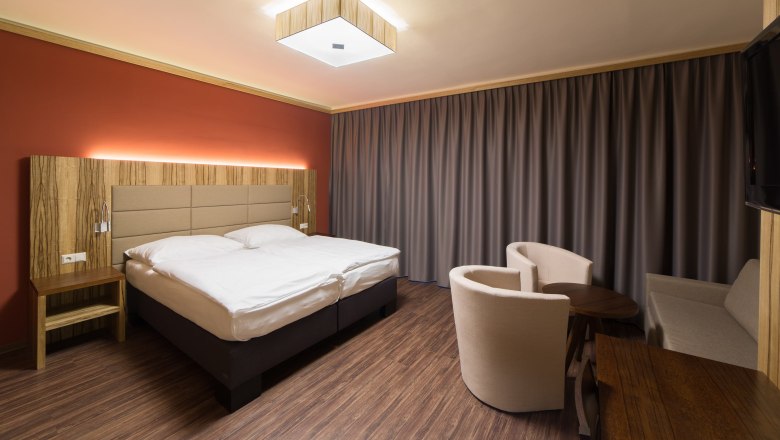 Modern eingerichtetes Hotelzimmer mit Doppelbett, Holzm&ouml;beln und Vorh&auml;ngen.