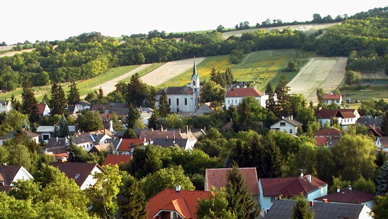 Landschaft mit Kirche und Dorf im Vordergrund, umgeben von Feldern und Hügeln.