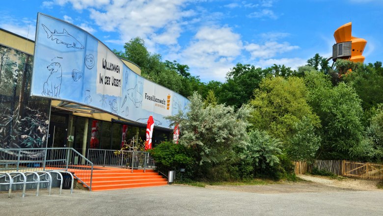 Eingang der Fossilienwelt mit einem großen Banner und Bäumen im Hintergrund.