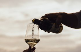 Wein wird in ein Glas im Freien eingeschenkt, im Hintergrund eine Landschaft.