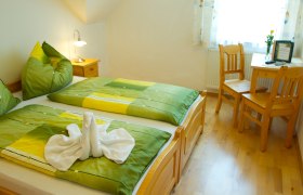 Gemütliches Gästezimmer mit Doppelbett, grüner Bettwäsche und Holzmöbeln.