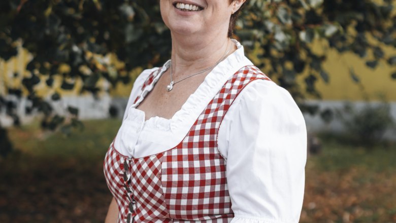 Frau in traditioneller Tracht vor einem Baum im Freien.