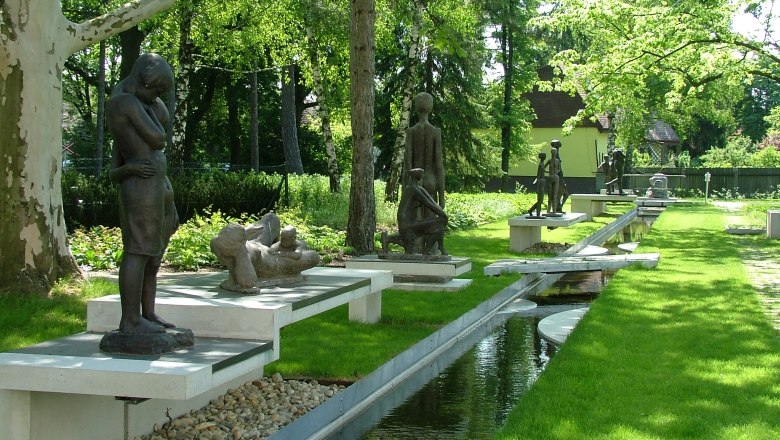 Skulpturengarten mit mehreren Bronzefiguren und einem Wasserlauf.
