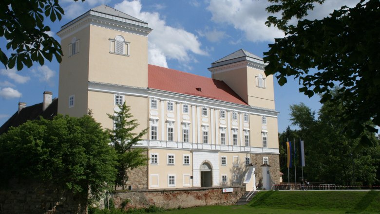 Schloss Wolkersdorf mit zwei Türmen und rotem Dach, umgeben von Bäumen.