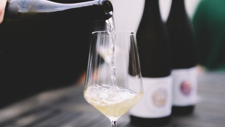 Wei&szlig;wein wird in ein Glas auf einem Tisch eingeschenkt.