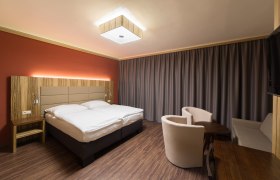 Modern eingerichtetes Hotelzimmer mit Doppelbett, Holzm&ouml;beln und Vorh&auml;ngen.