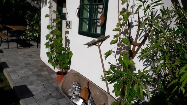 Weißes Gebäude mit grünen Fensterläden, Pflanzen und Gartenwerkzeugen an der Wand.