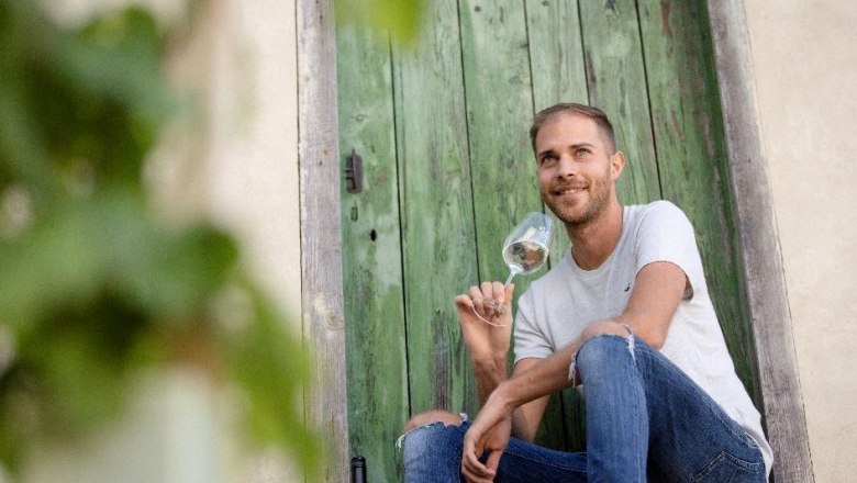 Ein Mann sitzt vor einer gr&uuml;nen Holzt&uuml;r und h&auml;lt ein Weinglas in der Hand.