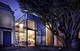 Moderne Glasfassade eines Geb&auml;udes bei Nacht, umgeben von B&auml;umen.