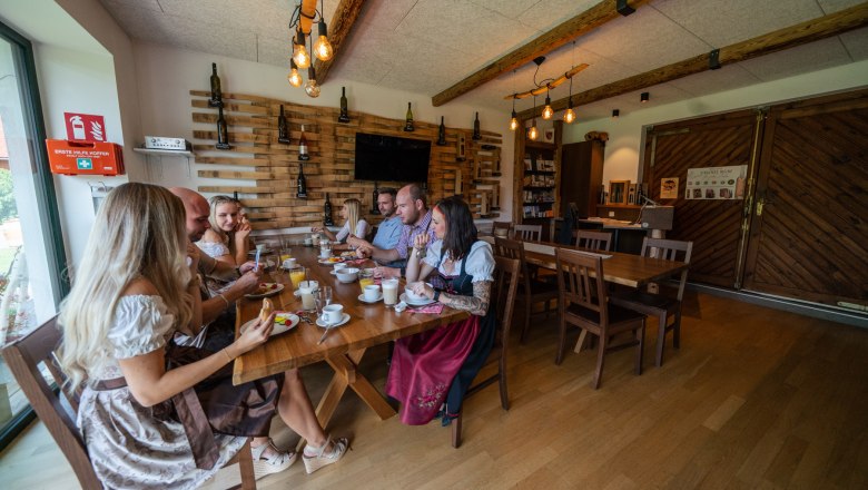 Gruppe von Menschen in traditioneller Kleidung sitzt an einem Tisch in einem rustikalen Raum.