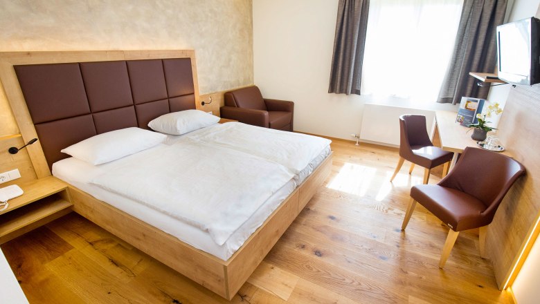 Modern eingerichtetes Hotelzimmer mit Doppelbett, Schreibtisch, St&uuml;hlen und einem Sessel.