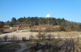 Landschaft mit Hügel, Wald und Radarkuppel unter blauem Himmel.