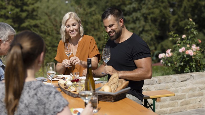 Gruppe von Menschen sitzt an einem Tisch im Freien und genießt Wein und Brot.