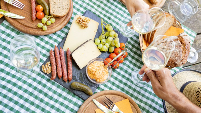 Picknick mit K&auml;se, Wurst, Brot und Wein auf kariertem Tischtuch.