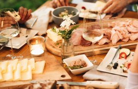 Ein gedeckter Tisch mit Brot, K&auml;se, Aufschnitt und Weingl&auml;sern.