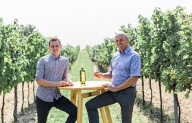 Zwei Männer sitzen an einem Tisch im Weinberg mit Weingläsern.
