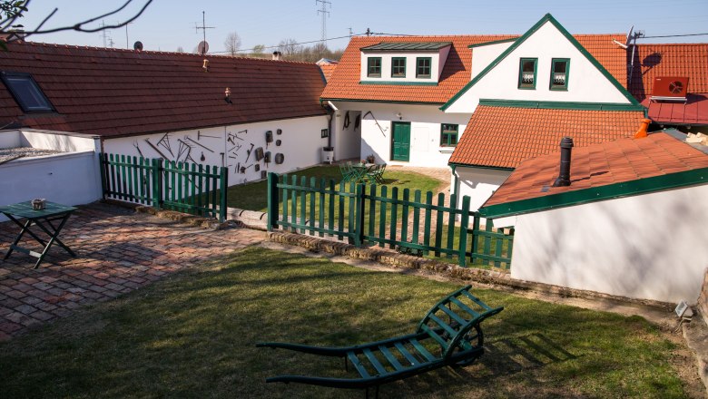 Ein traditioneller Winzerhof mit roten Ziegeldächern, grünen Zäunen und Gartenmöbeln auf einer Wiese.