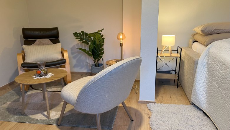 Gemütliches Schlafzimmer mit Sessel, Tisch, Pflanze und Bett.
