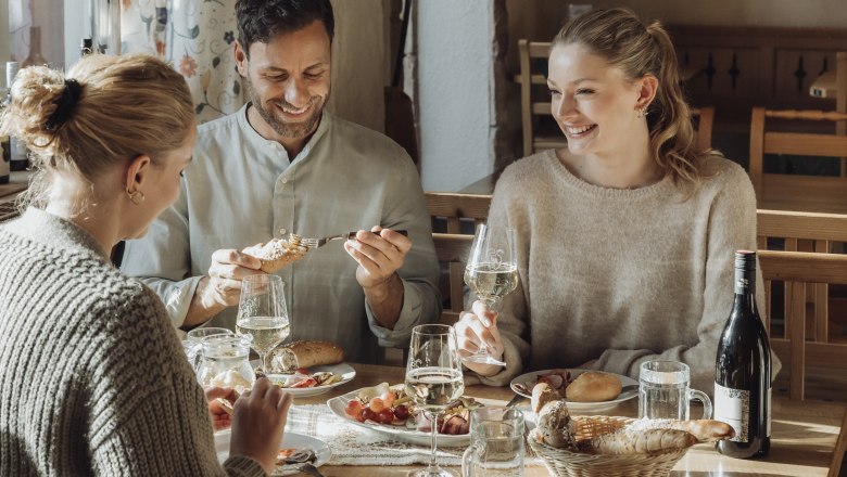 Drei Personen sitzen an einem Tisch in einem gemütlichen Restaurant und genießen Wein und Essen.