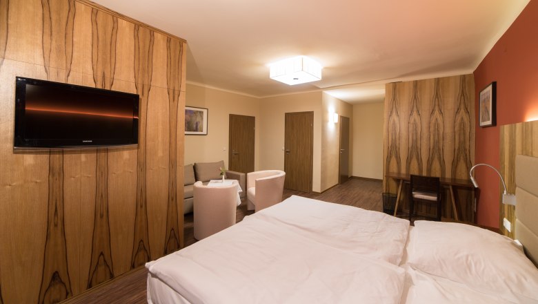 Modern eingerichtetes Hotelzimmer mit Doppelbett, Fernseher, Sitzbereich und Holzm&ouml;beln.