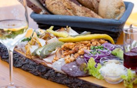 Heurigenplatte mit Wurst, Käse, Zwiebeln und Brot auf einem Holztisch.