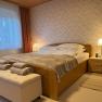 Gemütliches Schlafzimmer mit Doppelbett, Nachttischlampe und Fenster mit Vorhängen.