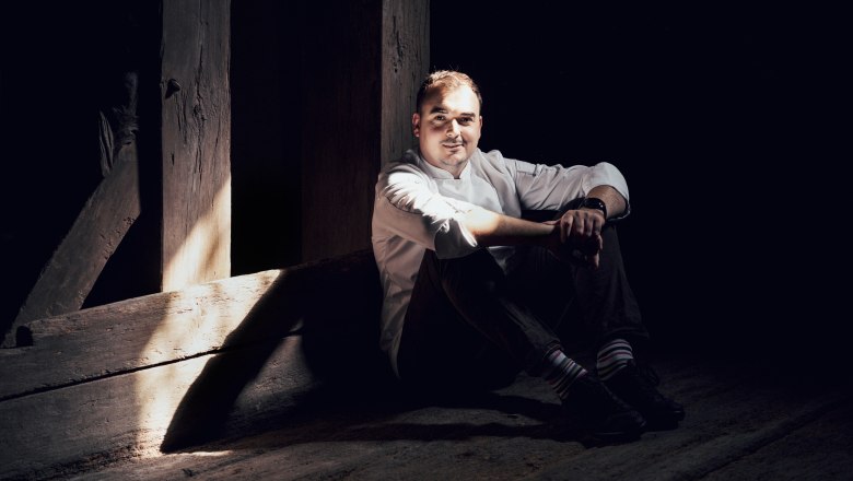 Mann in weißem Hemd sitzt im Schatten auf Holzboden.