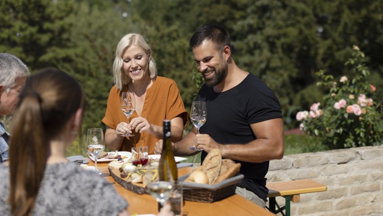 Gruppe von Menschen sitzt an einem Tisch im Freien und genießt Wein und Brot.