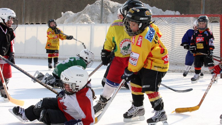 Kinder spielen Eishockey auf einer Außenbahn.